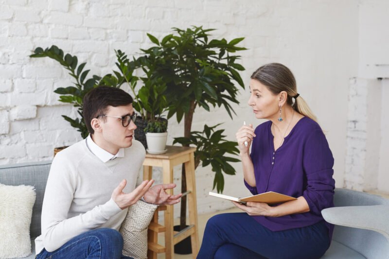 psychology therapy psychiatry mental health counseling concept candid shot nervous self conscious young male glasses telling middle aged female counselor about his problems work